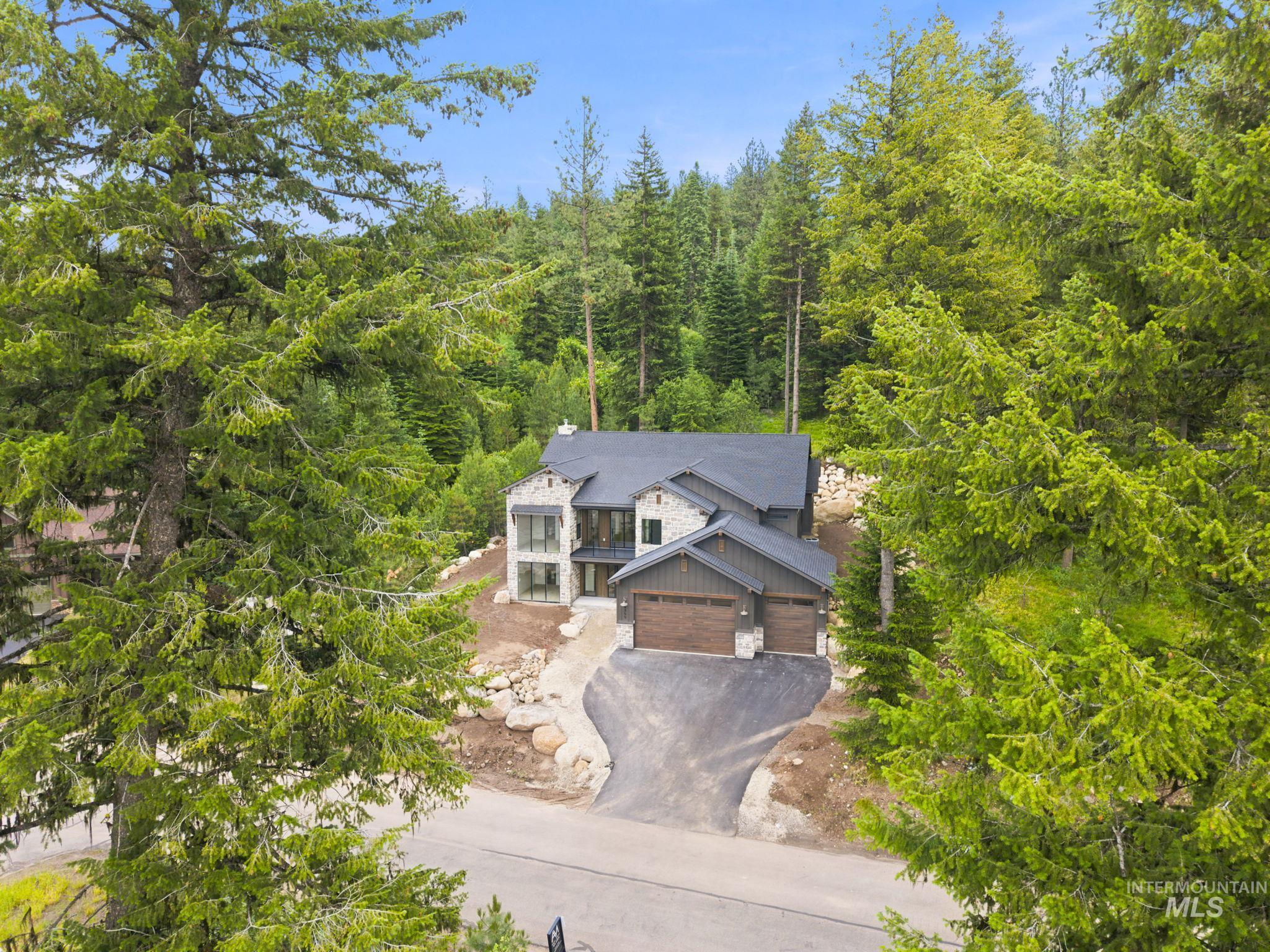 Contemporary architectural style featuring a stone and siding facade, a dark shingled roof, and a two-car garage with wood-finish doors