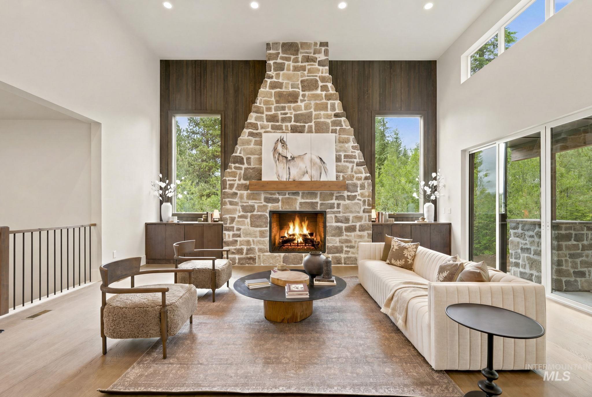 Double-height living space featuring a stone fireplace with a wood mantel, wood-finish flooring, and recessed lighting