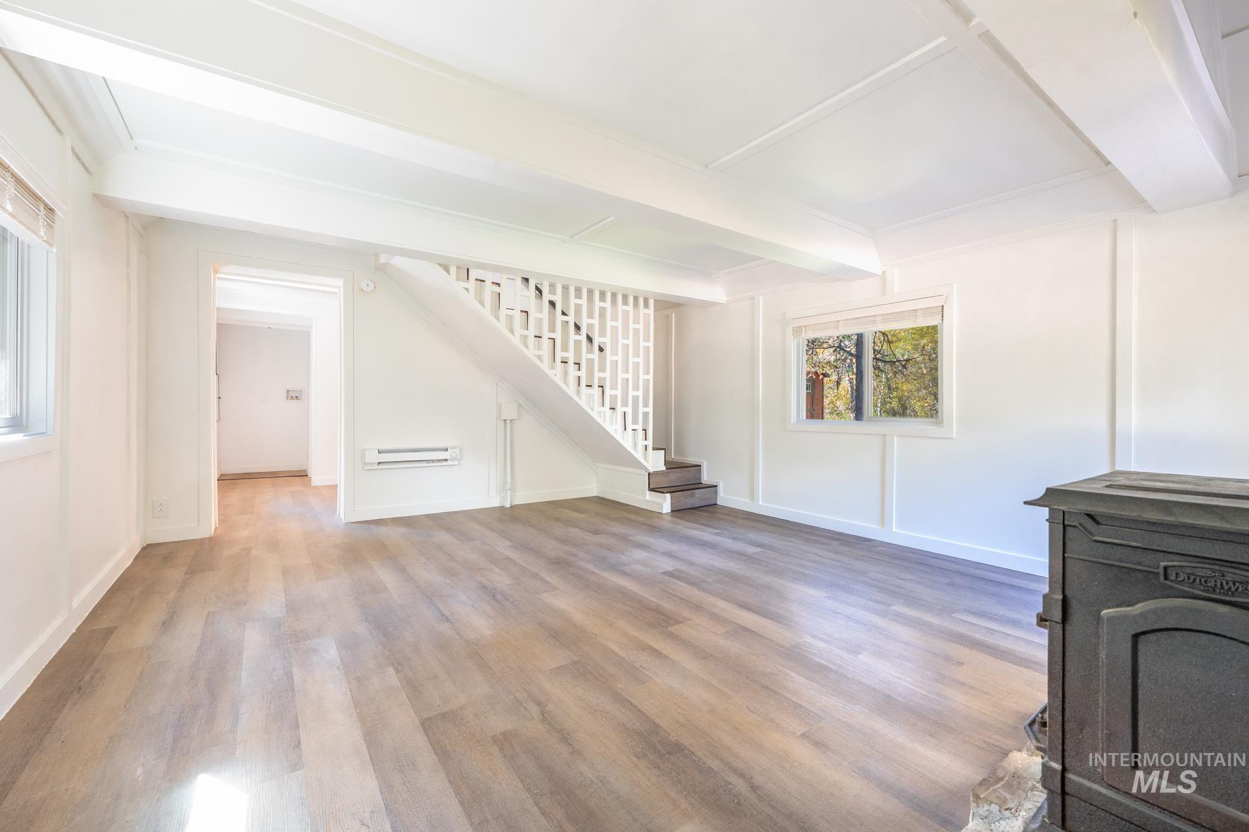 Unfurnished living room with beam ceiling, light wood finished floors, stairway, a wood stove, and baseboard heating