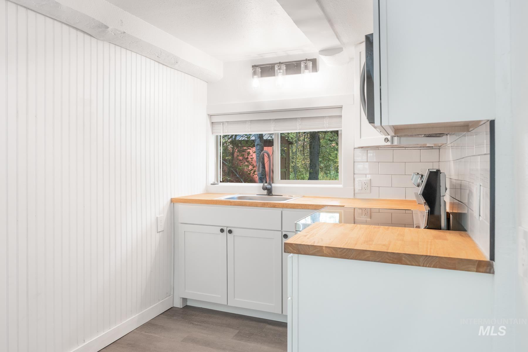 Kitchen with butcher block counters, white cabinetry, light wood-type flooring, and tasteful backsplash