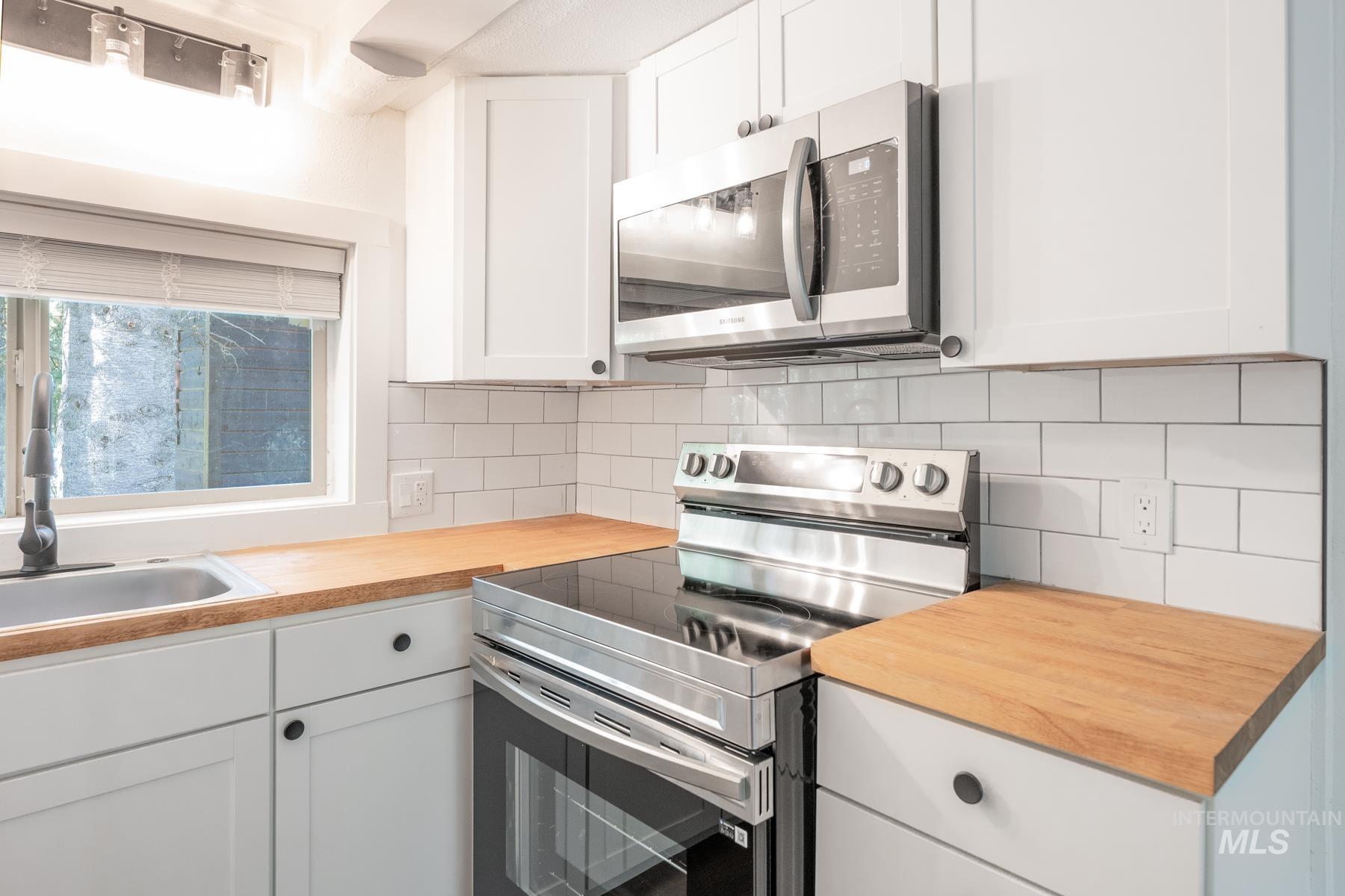 Kitchen featuring appliances with stainless steel finishes, white cabinets, backsplash, and wood counters