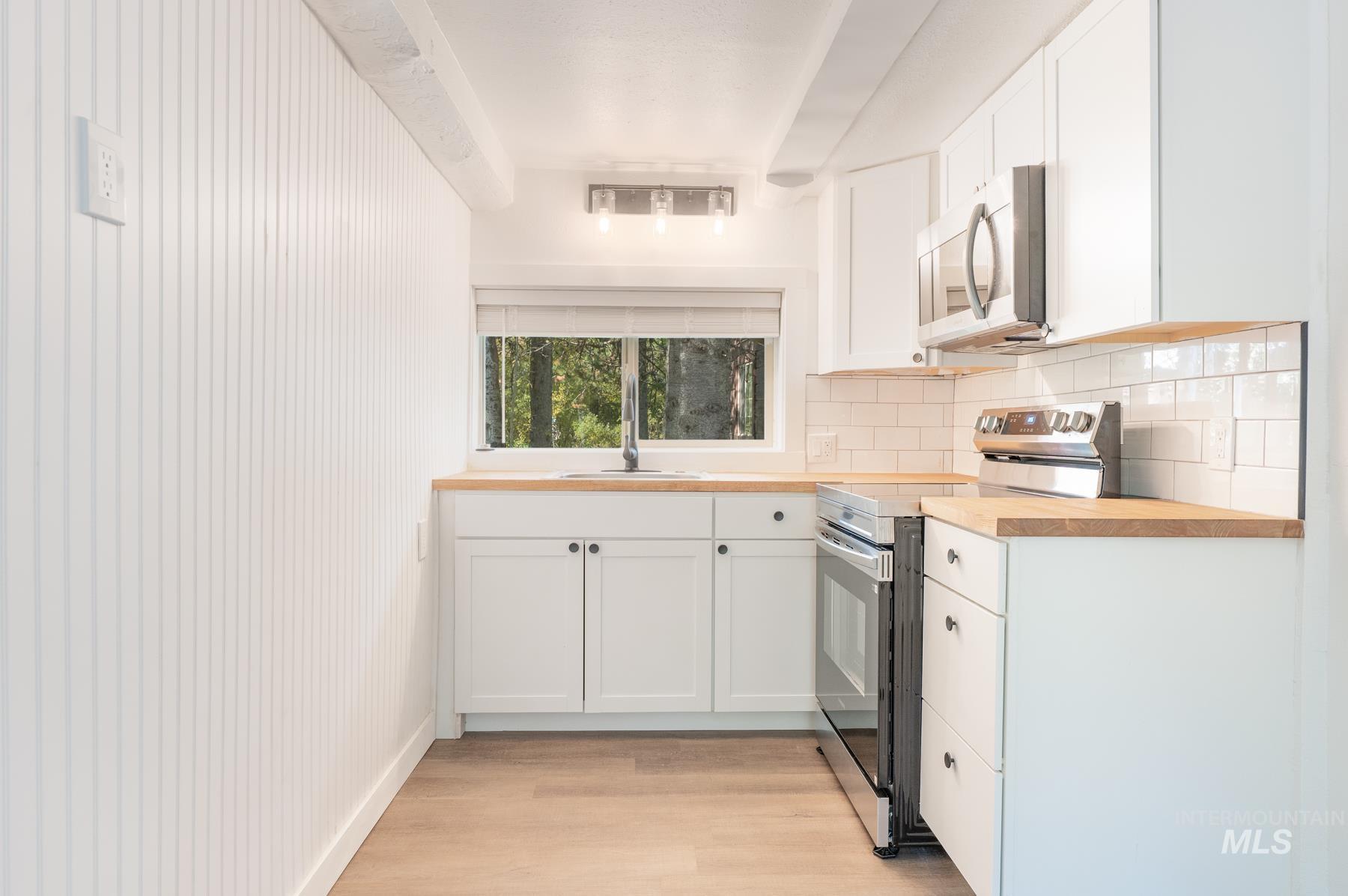 Kitchen featuring stainless steel appliances, white cabinetry, light wood-type flooring, backsplash, and wooden counters