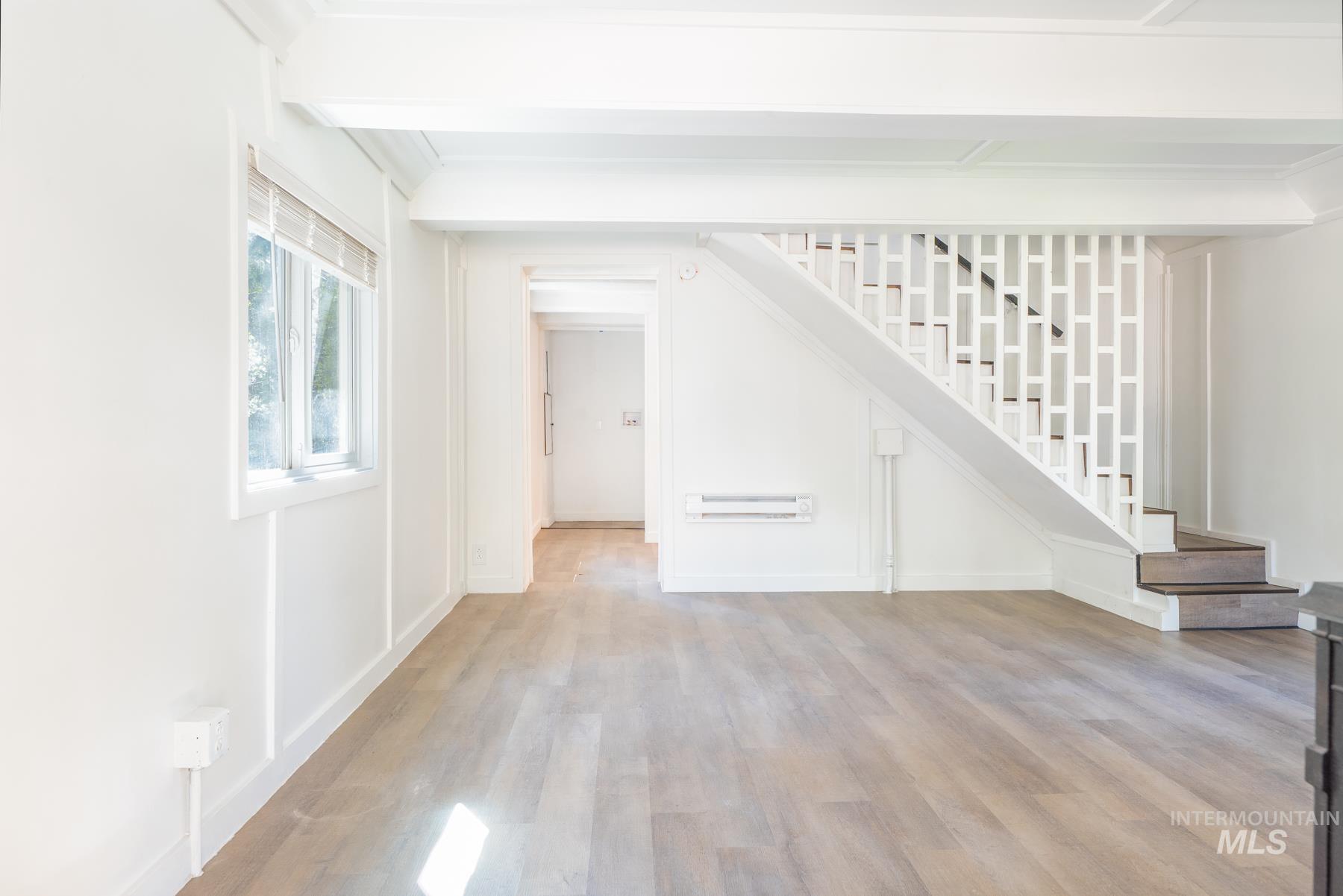 Unfurnished living room with light wood finished floors, stairs, and beam ceiling
