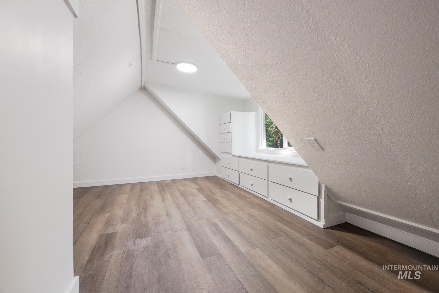 Additional living space featuring a textured ceiling, light wood-type flooring, and lofted ceiling