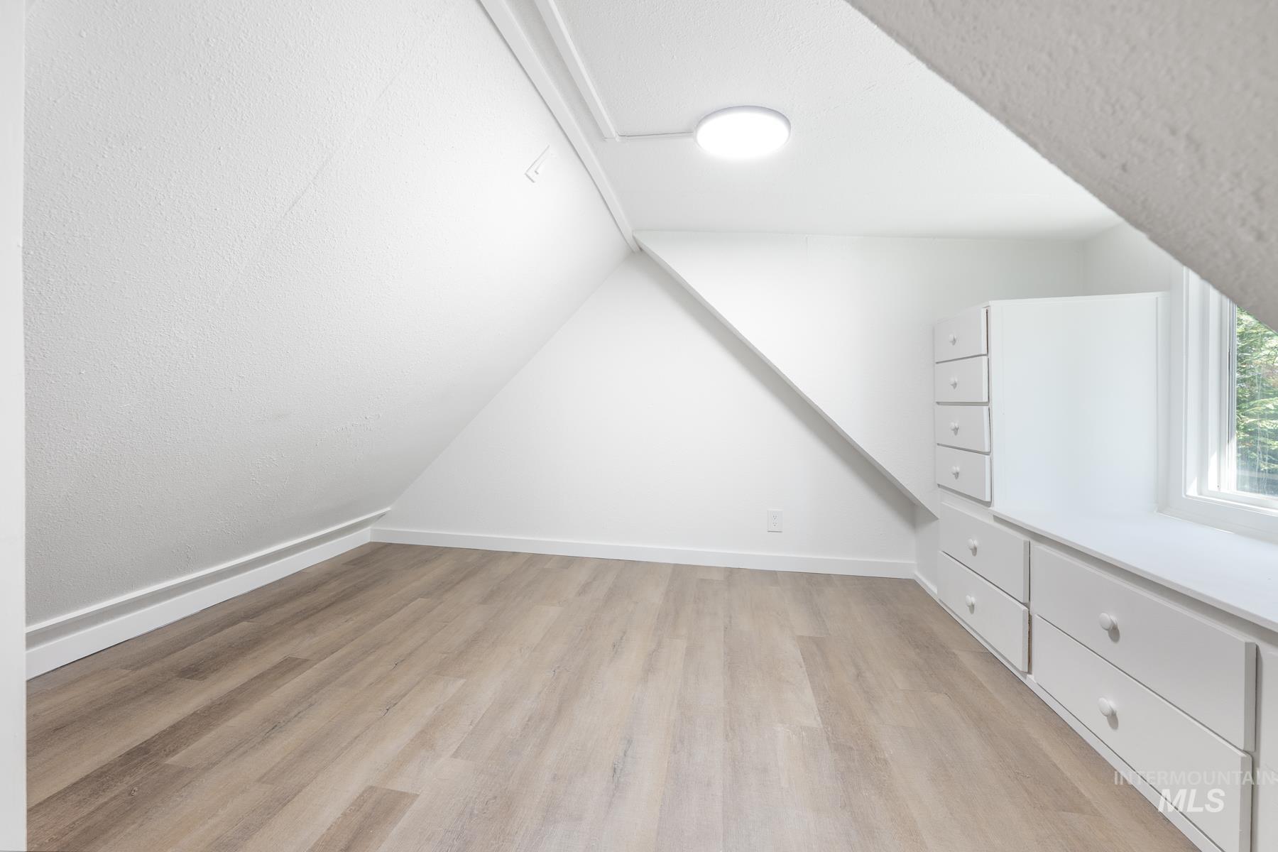 Additional living space featuring light wood-type flooring and lofted ceiling