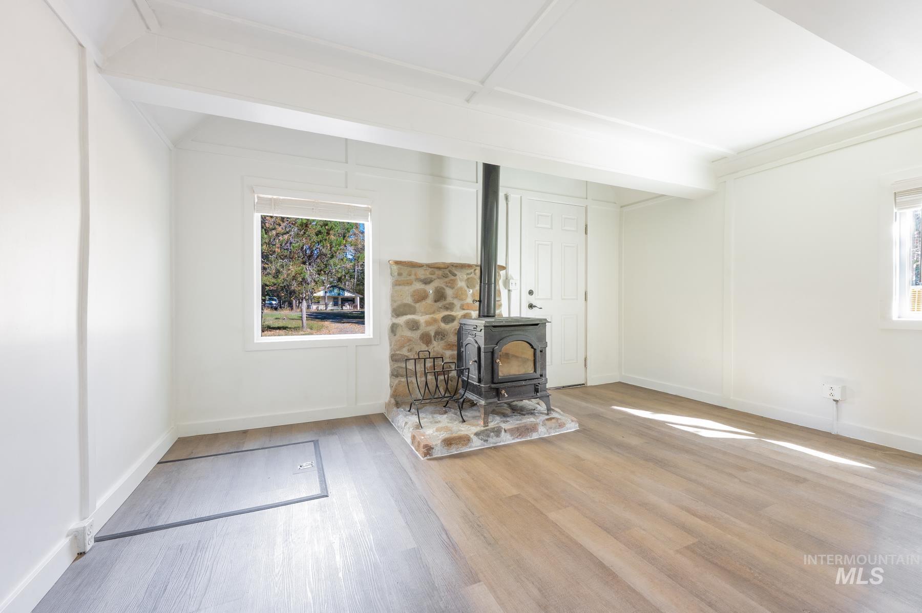 Unfurnished living room featuring a wood stove, light wood finished floors, and beamed ceiling