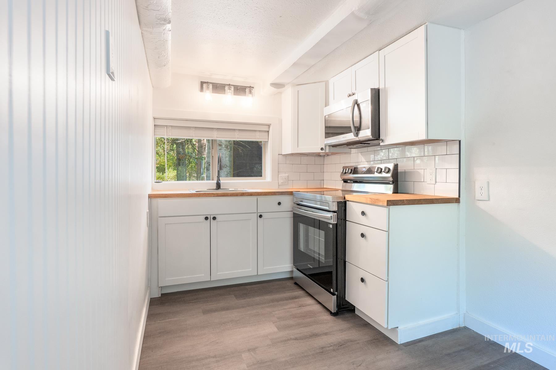 Kitchen featuring appliances with stainless steel finishes, white cabinets, butcher block counters, backsplash, and light wood-type flooring