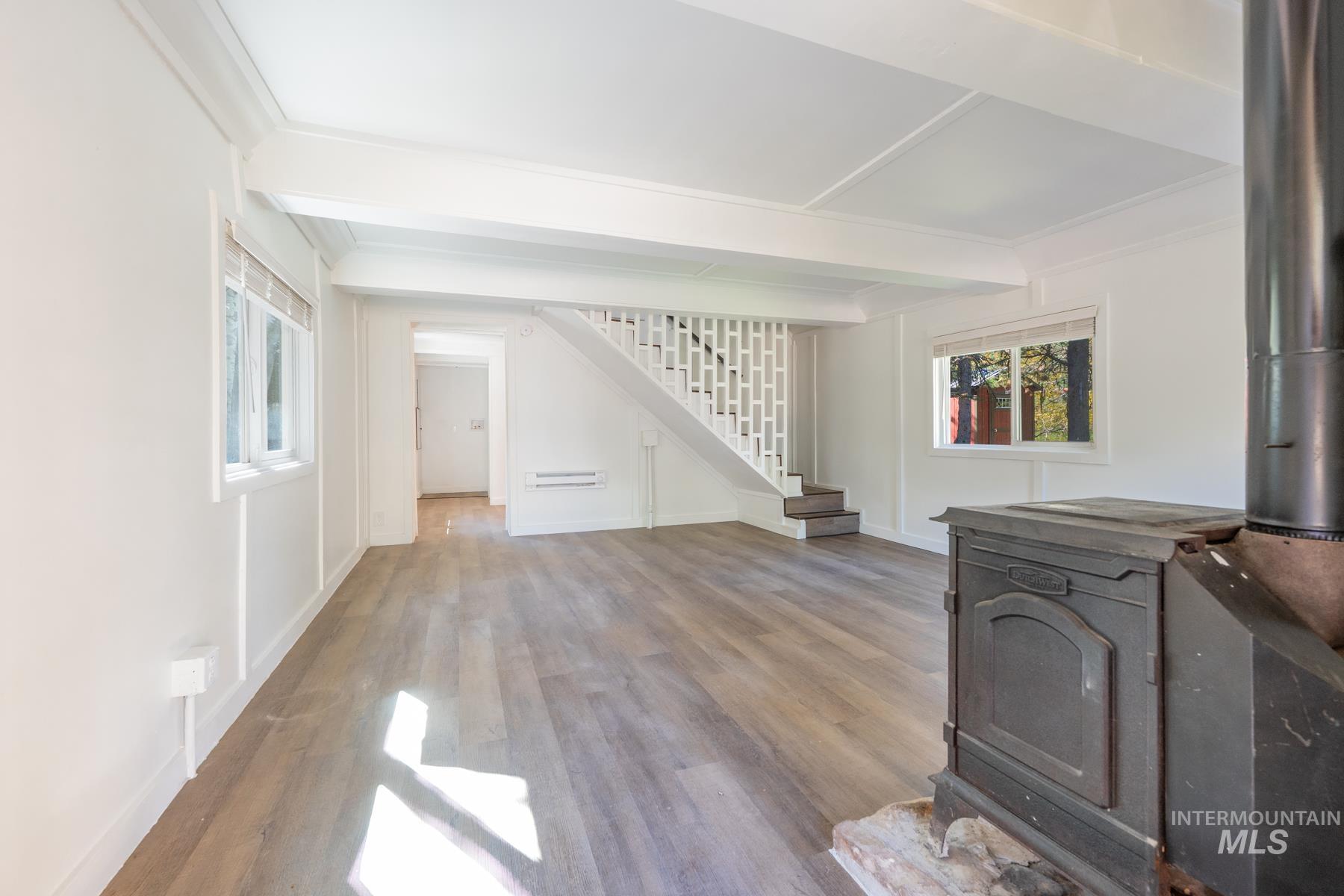 Unfurnished living room featuring a wood stove, beam ceiling, wood finished floors, stairs, and ornamental molding