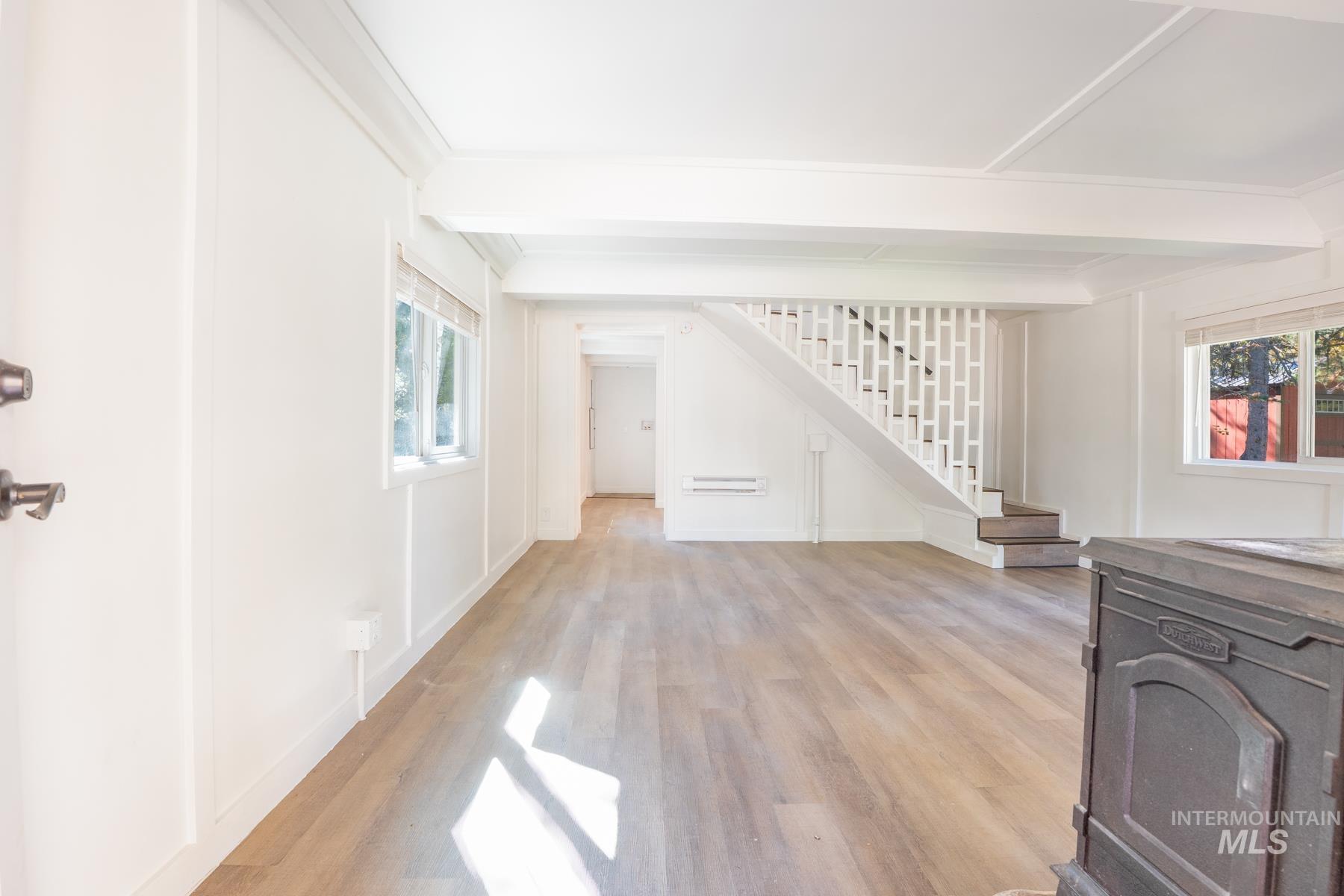 Unfurnished living room with beamed ceiling, light wood-style floors, stairs, and ornamental molding