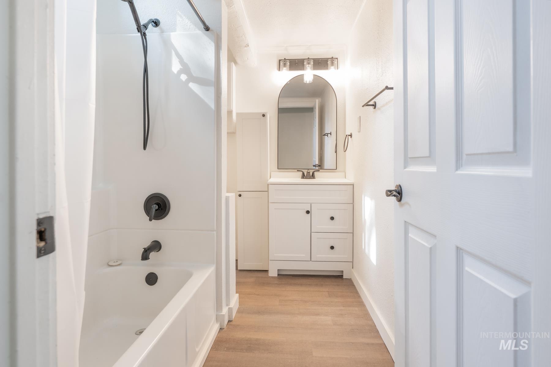 Bathroom with shower / bath combination, vanity, and light wood-style flooring