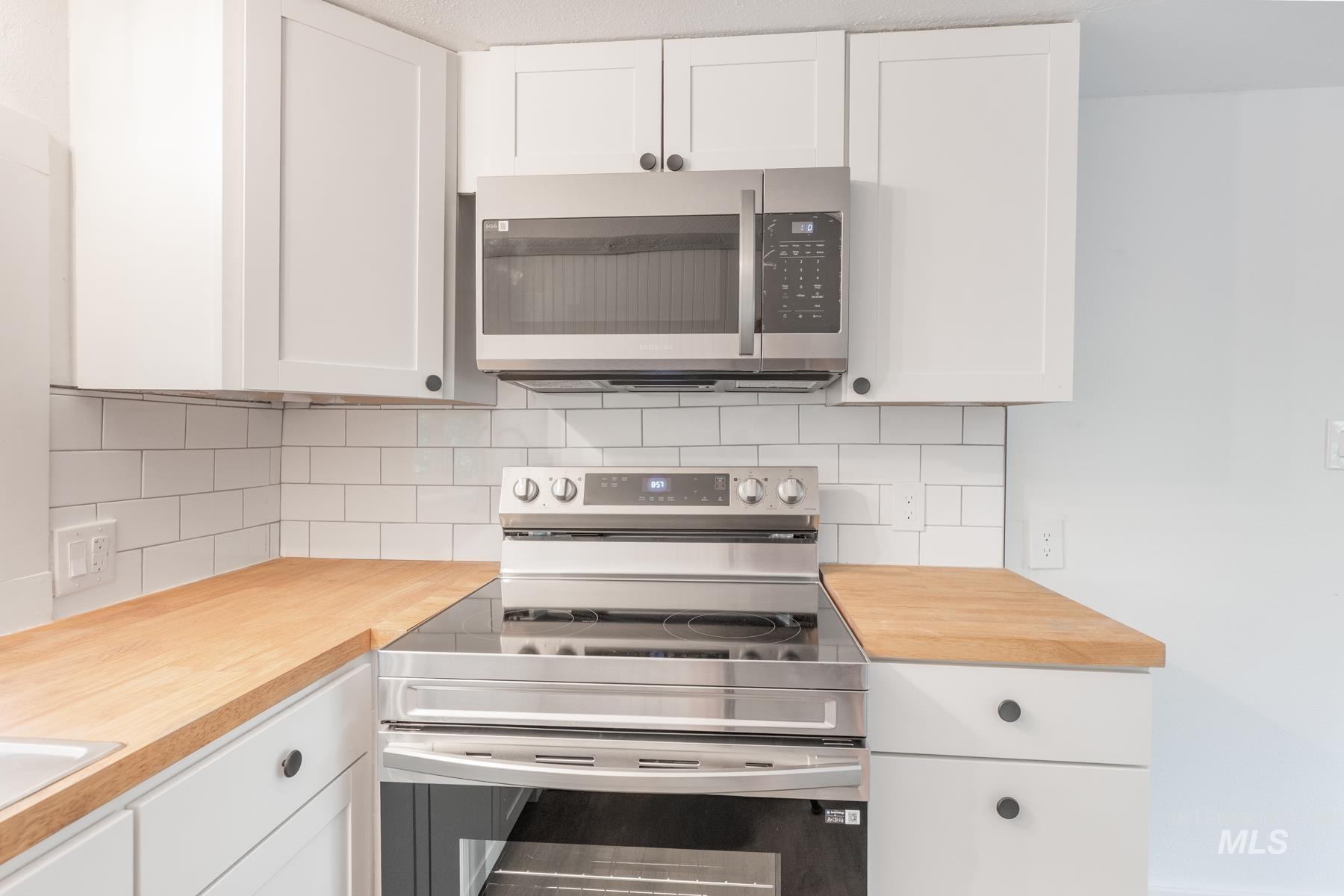 Kitchen featuring appliances with stainless steel finishes, white cabinetry, butcher block countertops, and tasteful backsplash