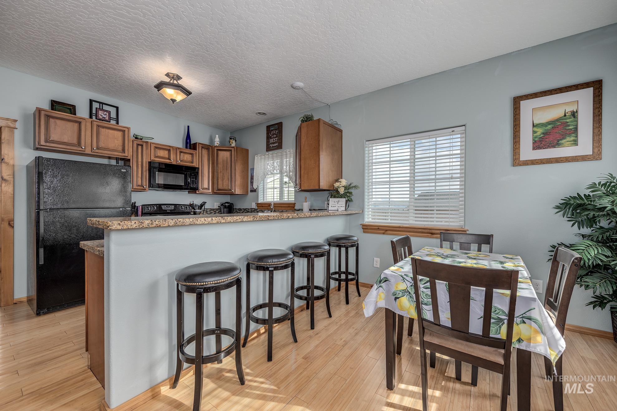 Guest house kitchen and dining area featuring black appliances, wood finish cabinetry, a peninsula, a textured ceiling, and light wood-style floors