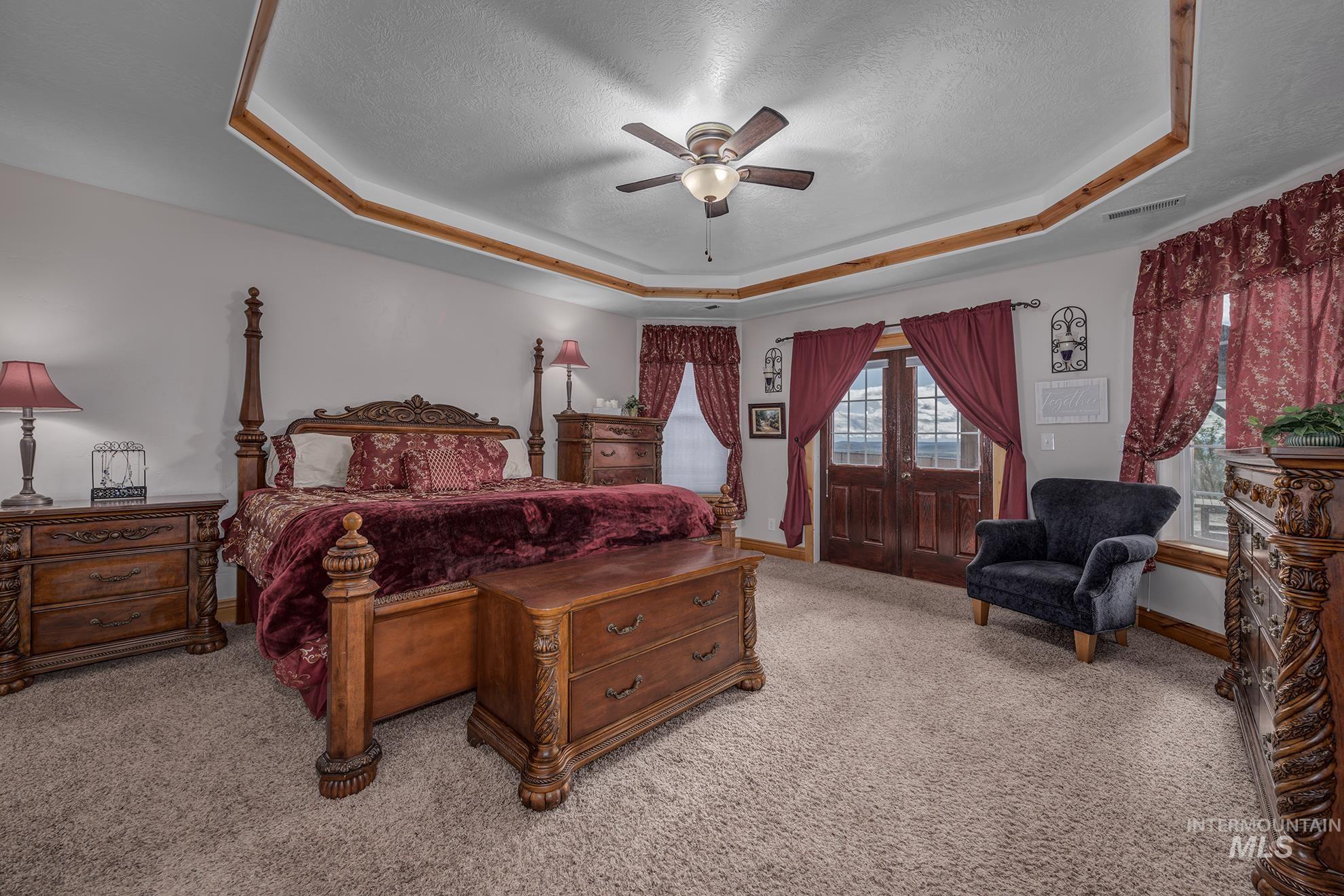 Master bedroom featuring french doors, light colored carpet, ceiling fan, a textured ceiling, and a tray ceiling