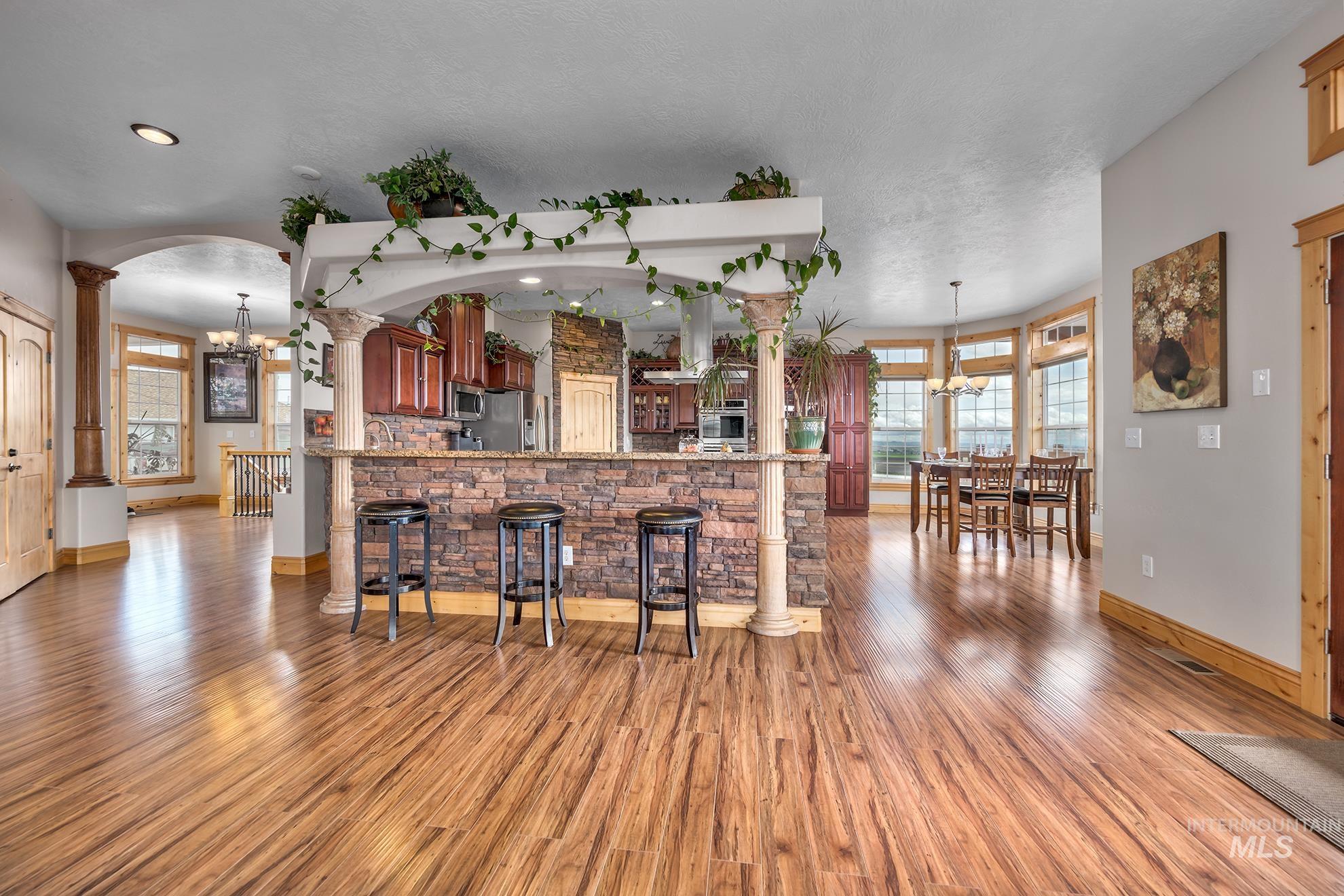 Kitchen featuring hanging lights, ornate columns, light wood-type flooring, a breakfast bar, and stainless steel appliances