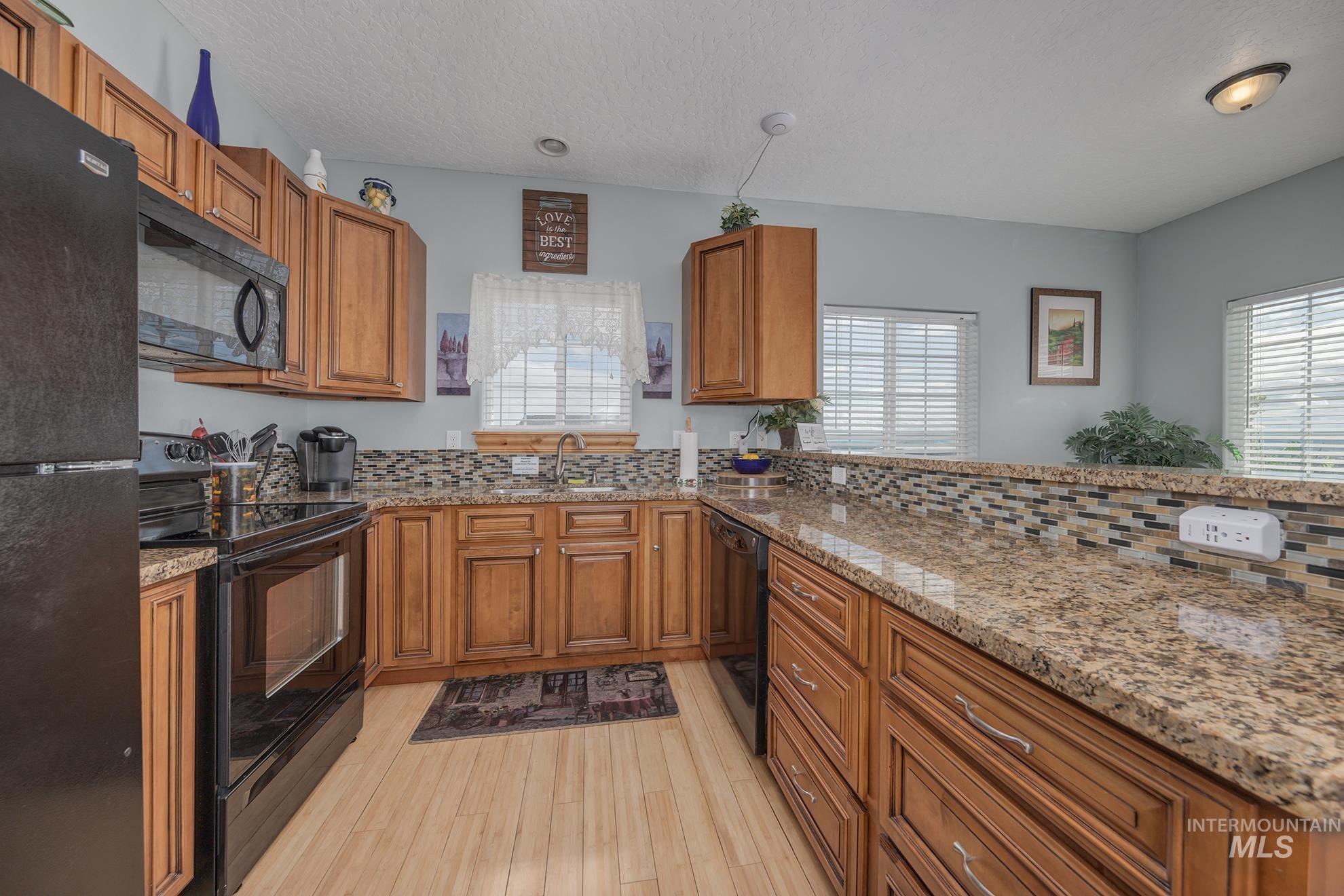 Guest house kitchen featuring black appliances, wood finish cabinetry, light stone counters, light wood-style floors, and healthy amount of natural light