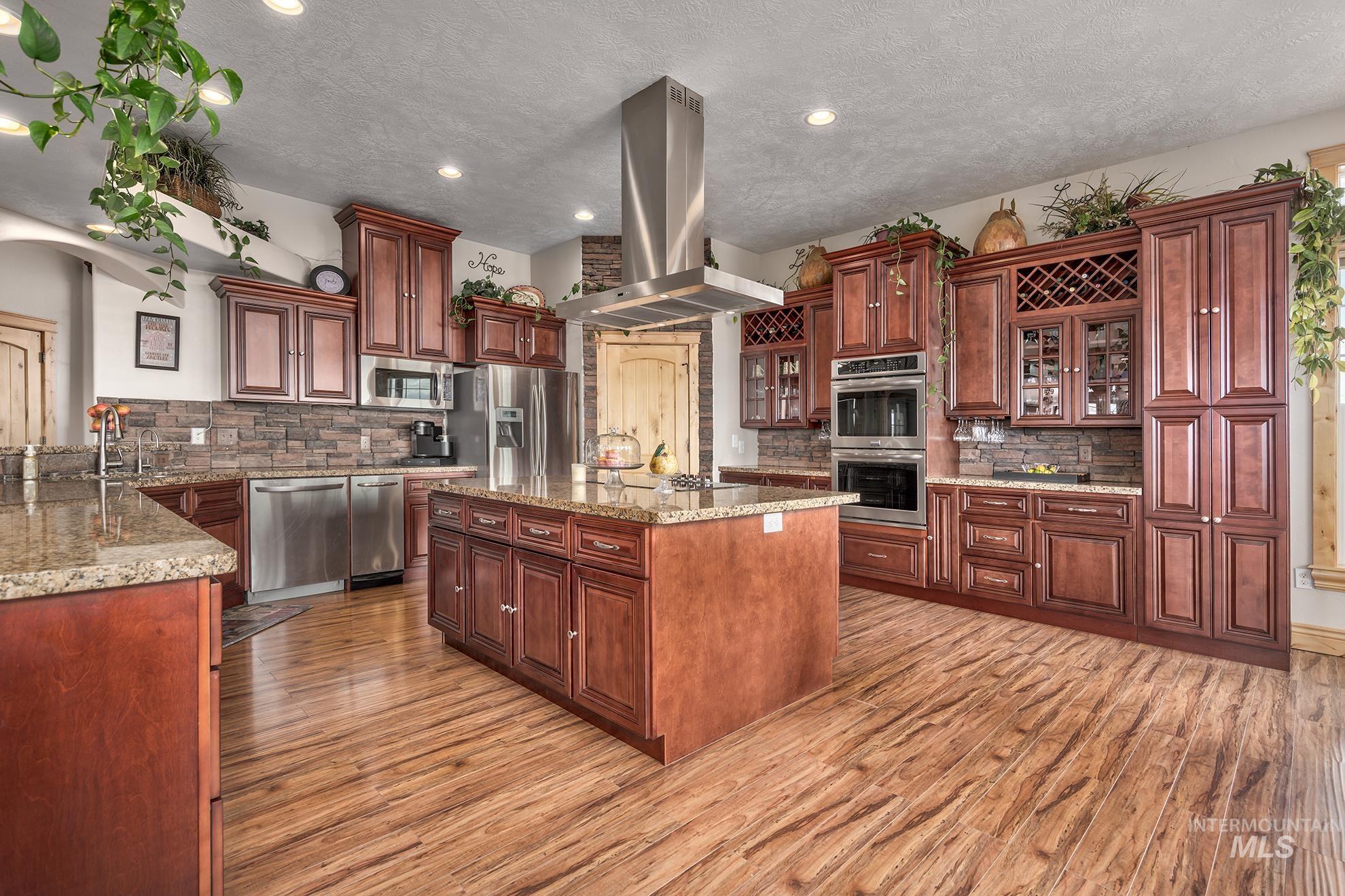 Kitchen featuring island exhaust hood, stainless steel appliances, glass fronted cabinets, light wood-style flooring, and a textured ceiling