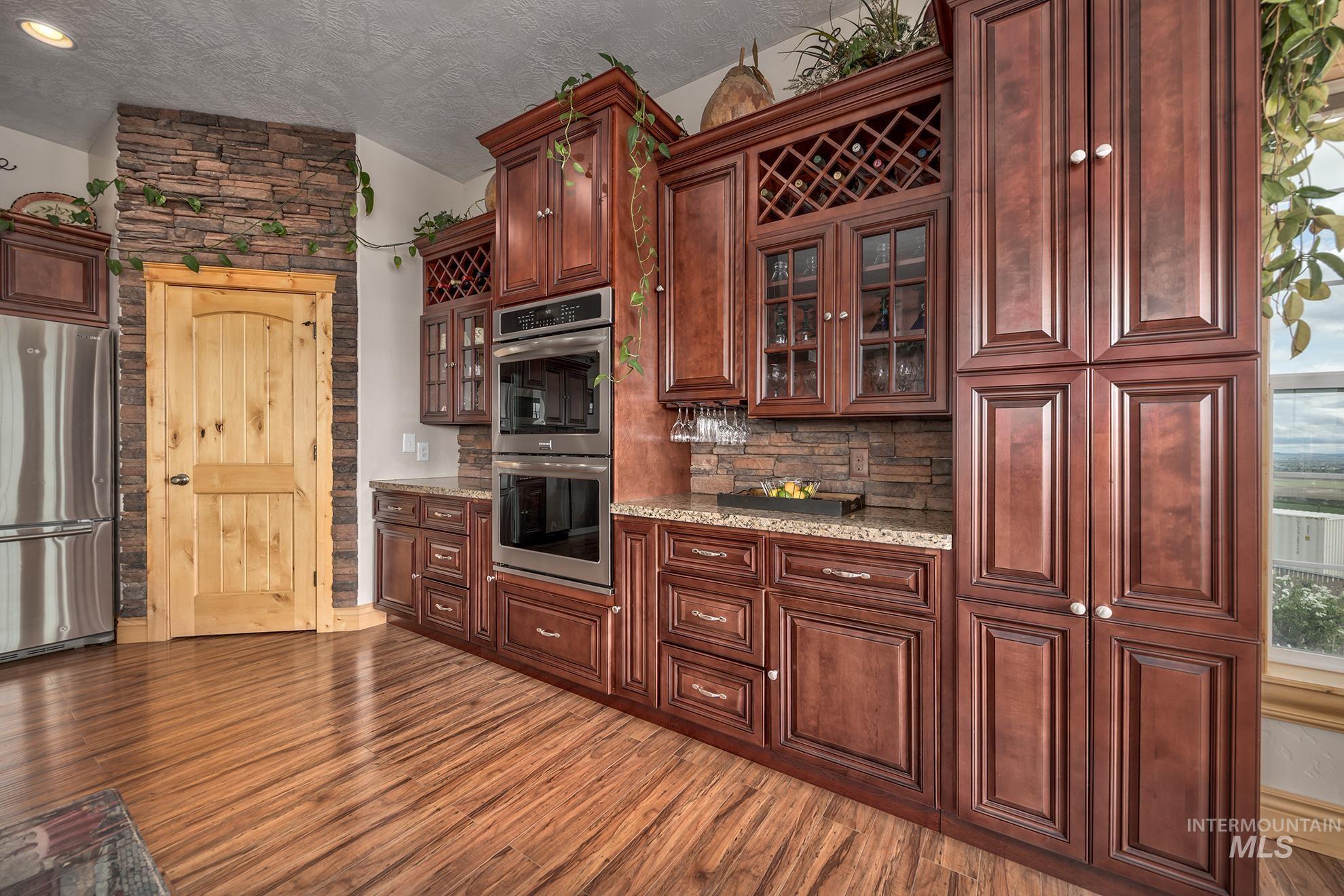 Kitchen featuring stainless steel appliances, glass fronted cabinets, light stone counters, and dark wood-style floors