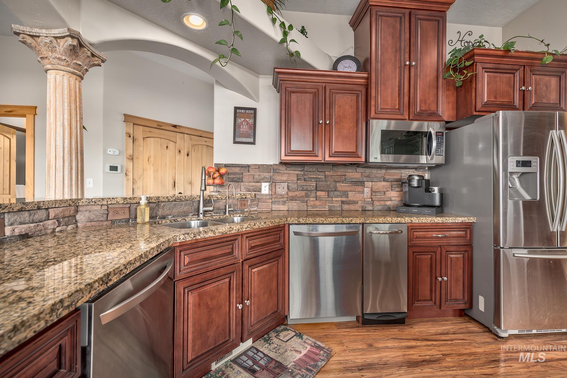 Kitchen featuring stainless steel appliances, light stone countertops, wood finished floors, and decorative backsplash