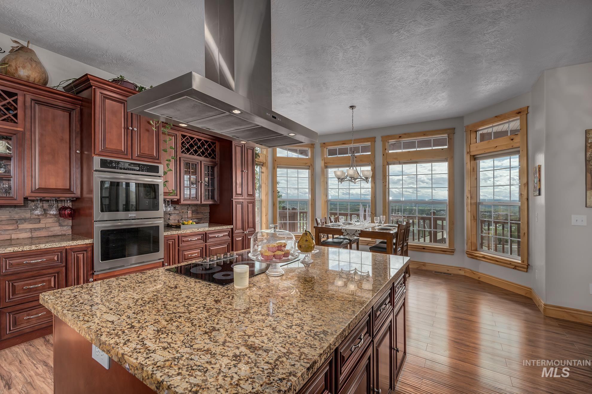 Kitchen with exhaust hood, glass fronted cabinets, stainless steel double oven, light stone countertops, and a textured ceiling