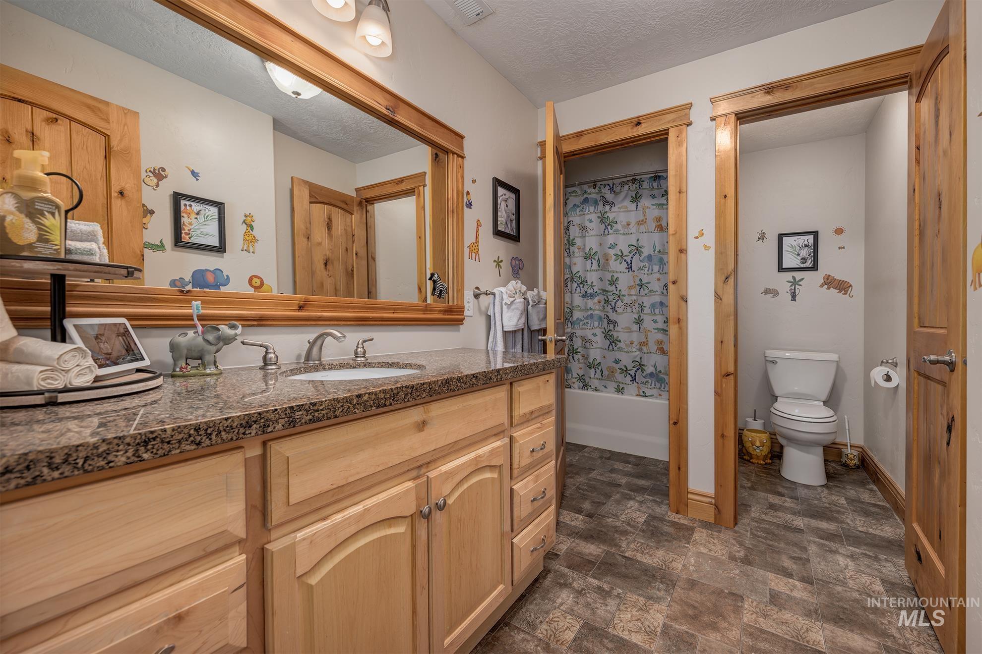 Full bath with stone finish floors, vanity, a textured ceiling, and shower / tub combo with curtain