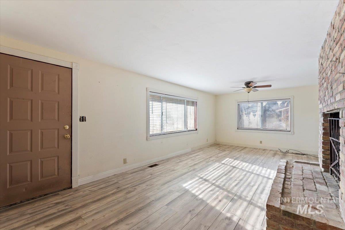 Unfurnished living room with a brick fireplace, plenty of natural light, wood finished floors, and a ceiling fan