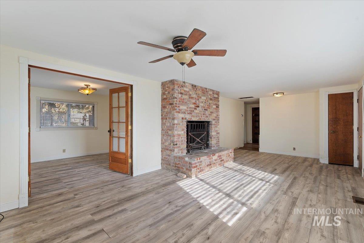Unfurnished living room featuring light wood-style floors, a brick fireplace, and ceiling fan
