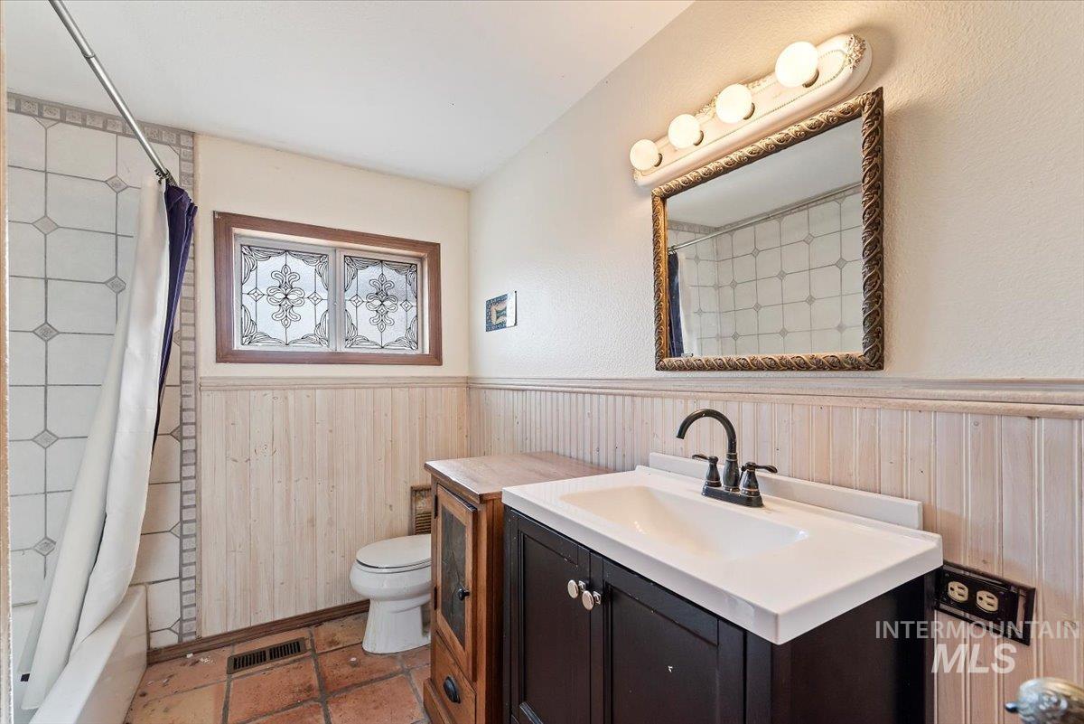 Full bath featuring a wainscoted wall, shower / tub combo with curtain, vanity, and wooden walls