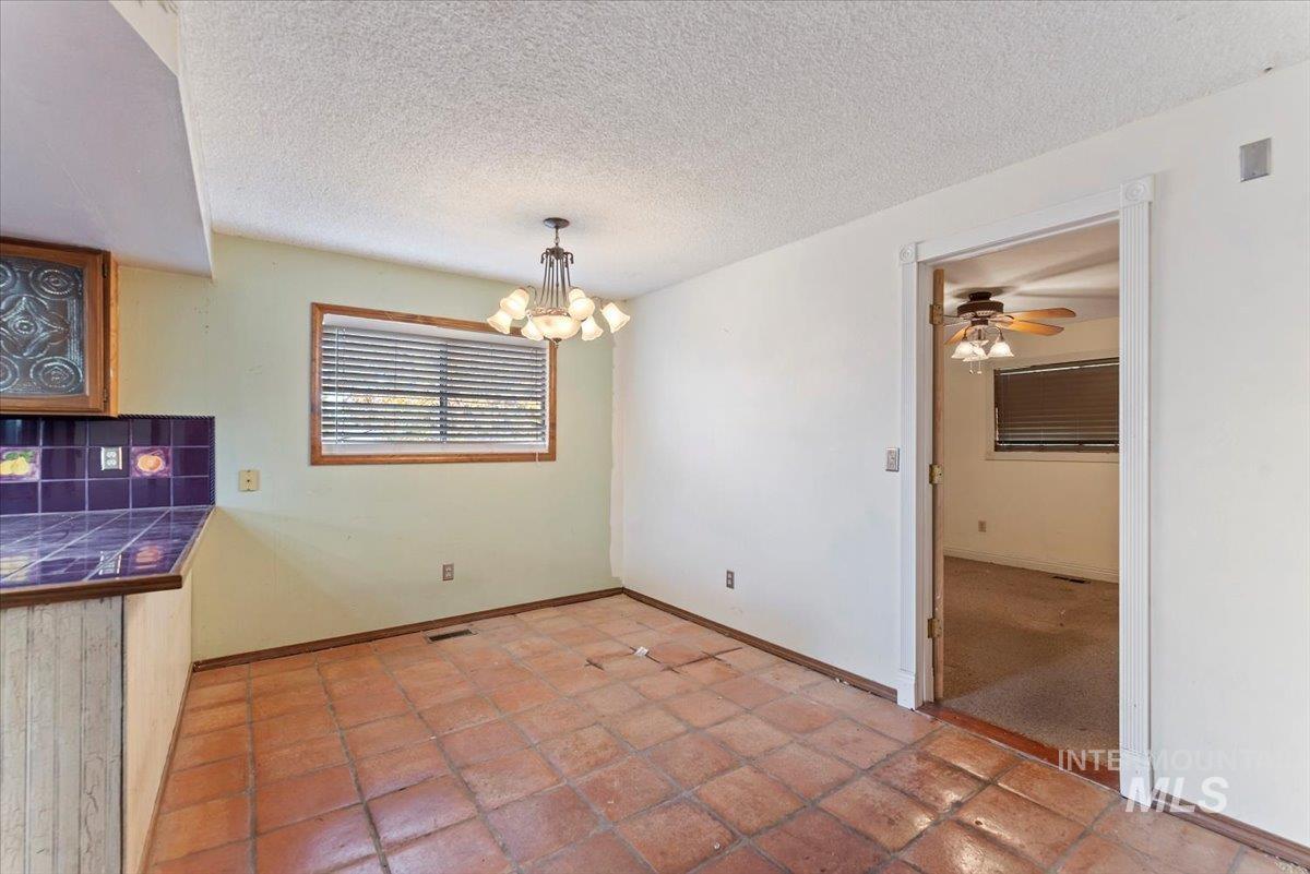Unfurnished dining area featuring a textured ceiling, a chandelier, ceiling fan, and light tile patterned flooring