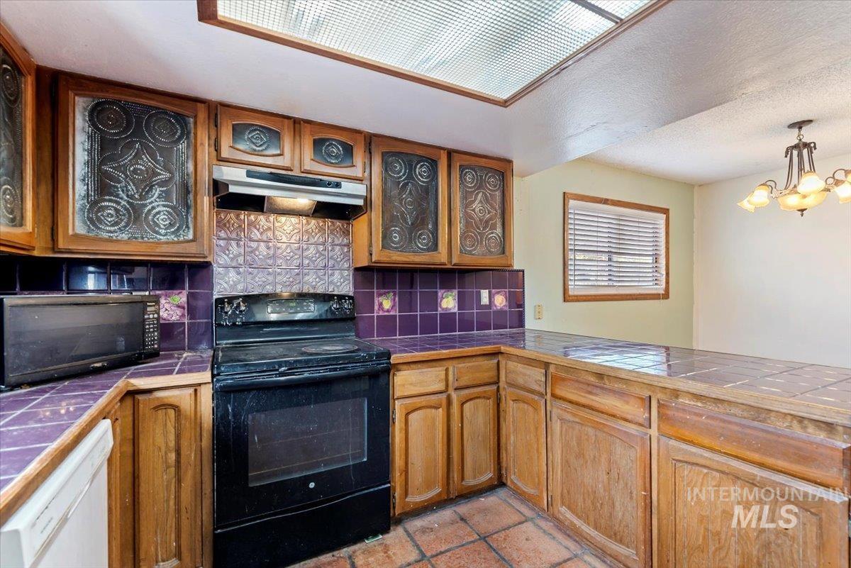 Kitchen featuring backsplash, black appliances, tile countertops, under cabinet range hood, and a textured ceiling