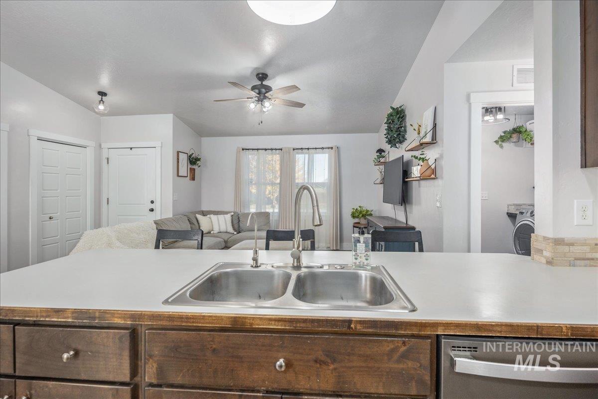 Kitchen with light countertops, stainless steel dishwasher, open floor plan, a ceiling fan, and dark brown cabinetry