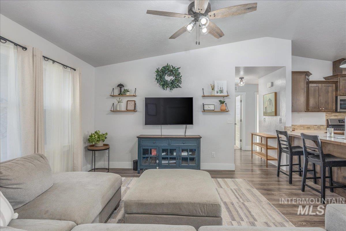 Living area featuring lofted ceiling, wood finished floors, a ceiling fan, and a textured ceiling