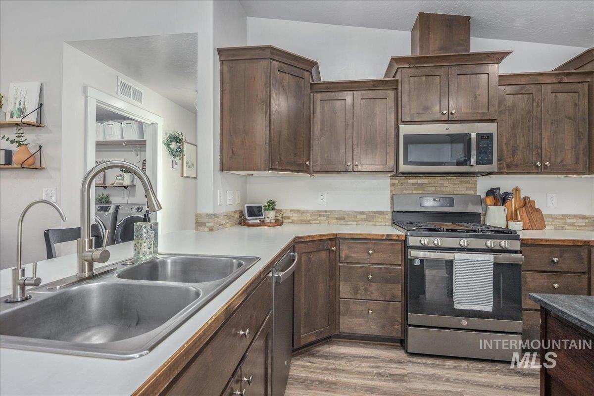 Kitchen featuring dark brown cabinets, stainless steel appliances, light wood-style floors, and light countertops