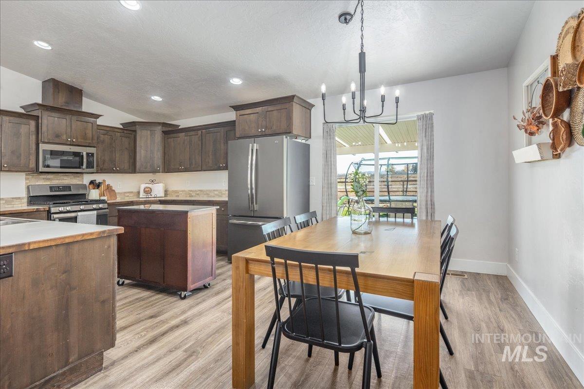 Kitchen featuring stainless steel appliances, dark brown cabinetry, light wood-style floors, a chandelier, and decorative light fixtures