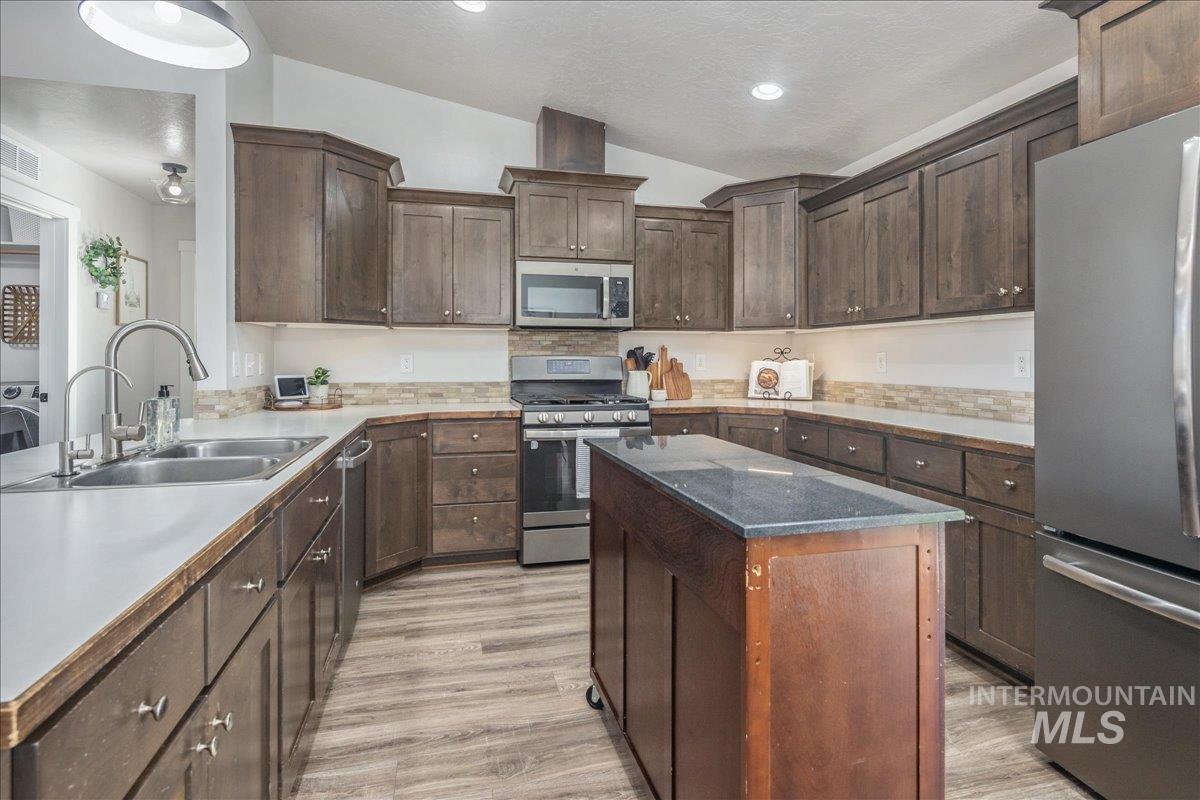 Kitchen featuring dark brown cabinetry, appliances with stainless steel finishes, a kitchen island, light wood-style flooring, and a textured ceiling