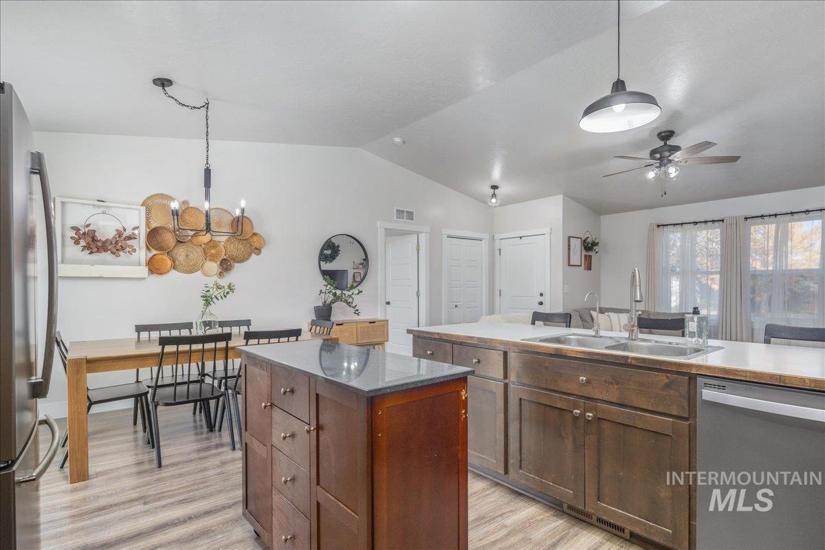 Kitchen featuring appliances with stainless steel finishes, lofted ceiling, decorative light fixtures, a kitchen island, and light wood-style flooring