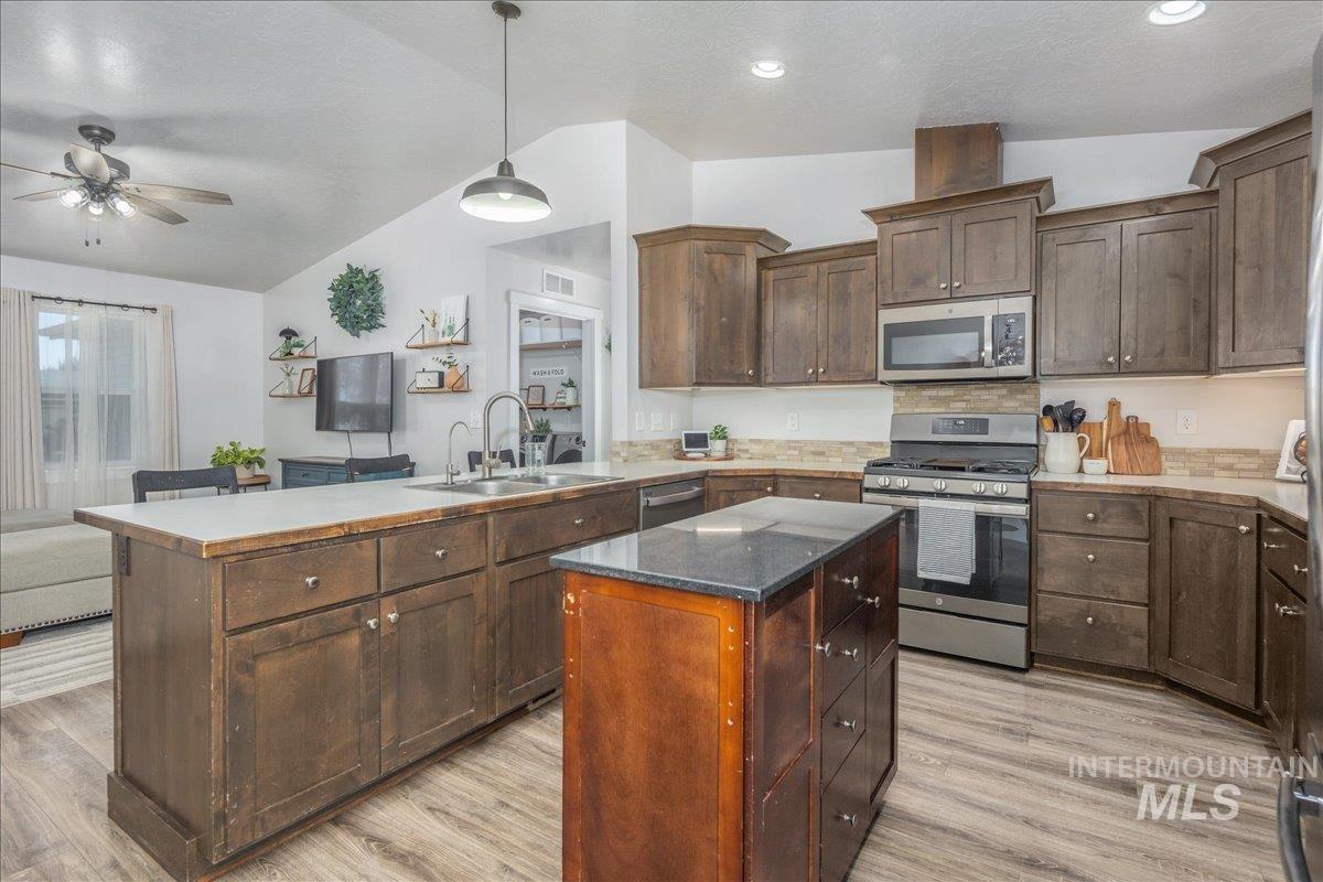 Kitchen featuring a peninsula, vaulted ceiling, appliances with stainless steel finishes, decorative light fixtures, and dark brown cabinetry