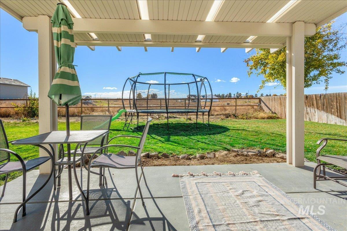 Fenced backyard with a trampoline, a patio area, and outdoor dining area