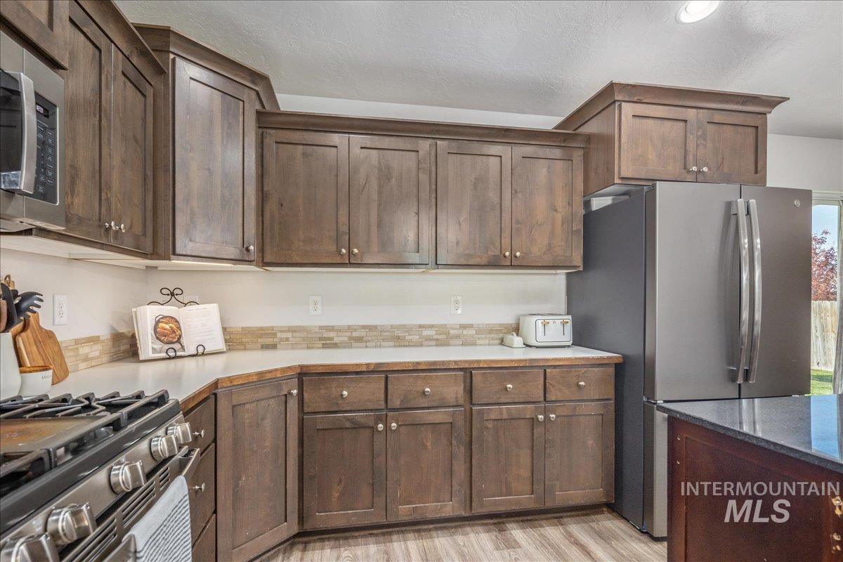 Kitchen featuring appliances with stainless steel finishes, dark brown cabinetry, light wood finished floors, and a textured ceiling