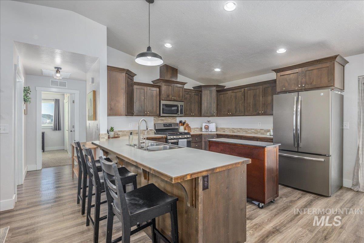 Kitchen with appliances with stainless steel finishes, lofted ceiling, light countertops, dark brown cabinets, and hanging light fixtures