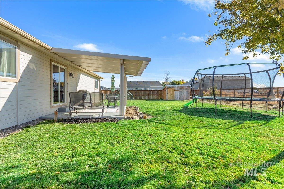 Fenced backyard featuring a trampoline, a patio, and a storage shed
