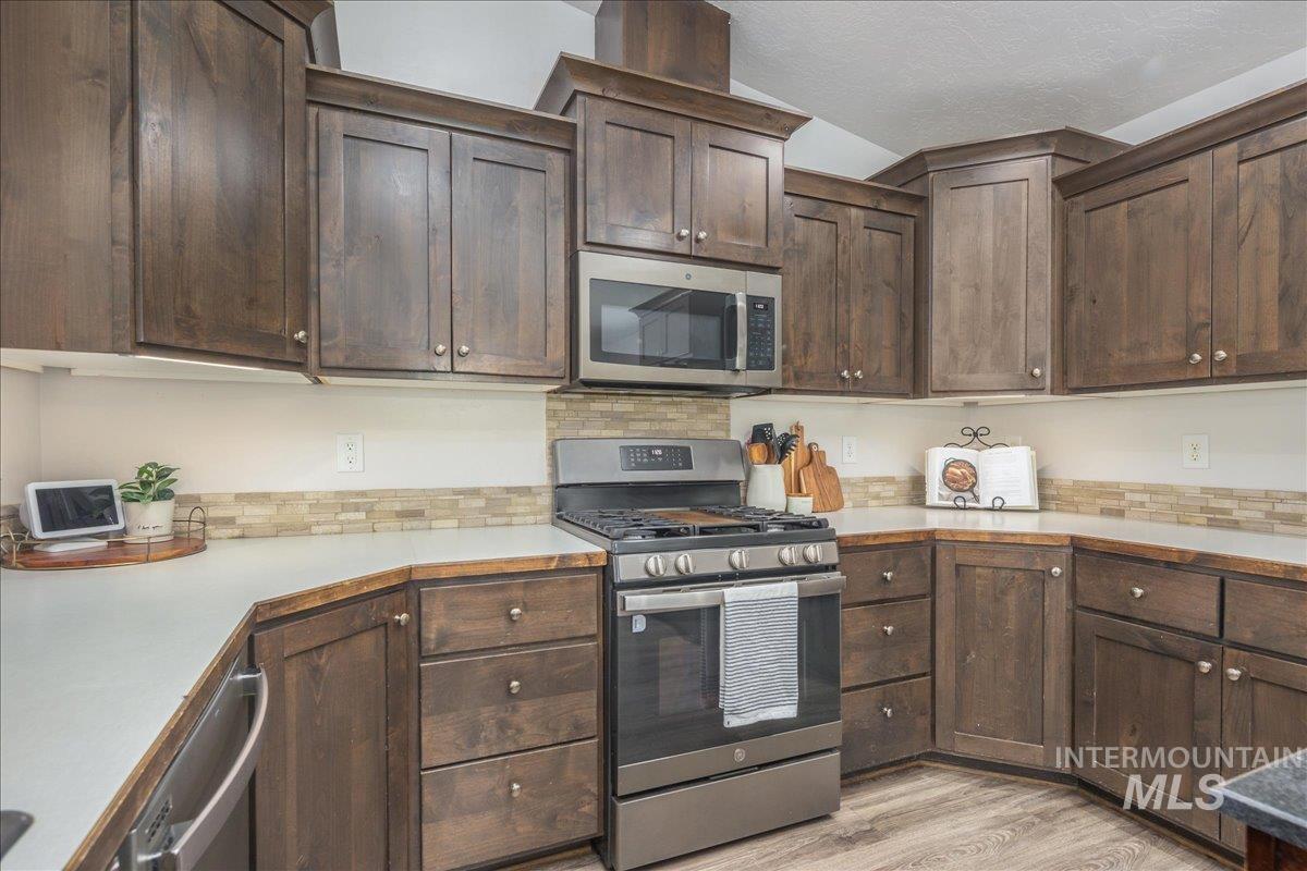 Kitchen featuring dark brown cabinets, stainless steel appliances, light countertops, light wood finished floors, and a textured ceiling