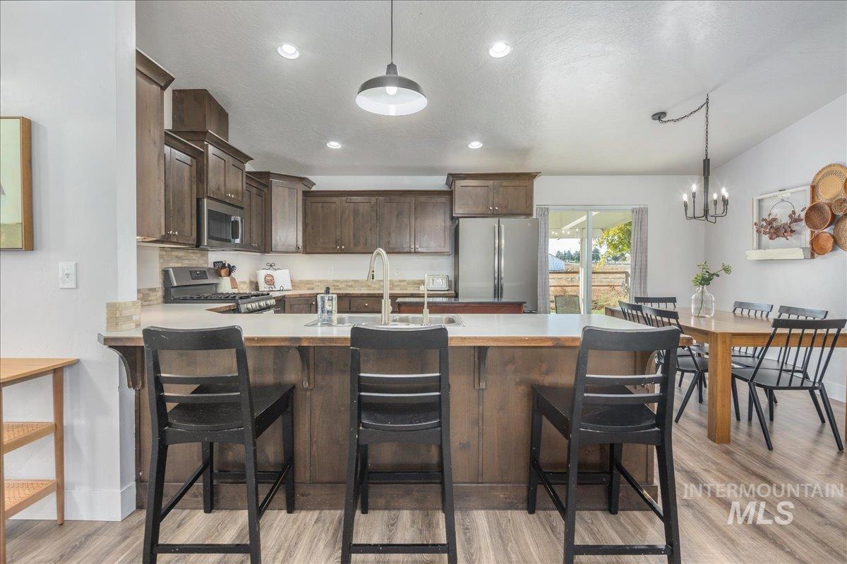 Kitchen featuring dark brown cabinets, light countertops, hanging light fixtures, recessed lighting, and stainless steel appliances