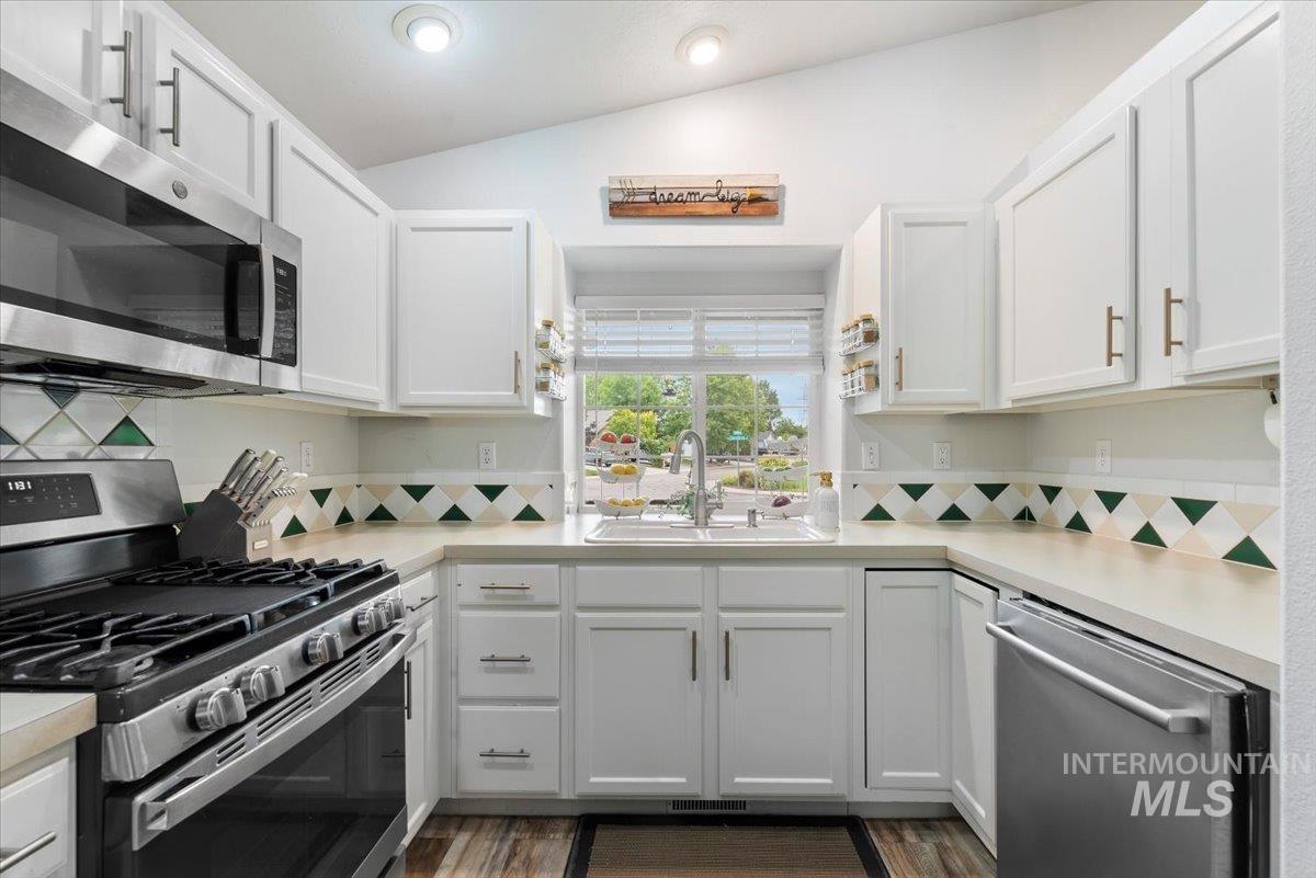 Bright kitchen featuring white cabinetry, light countertops, stainless steel appliances, and a tile backsplash with green accents