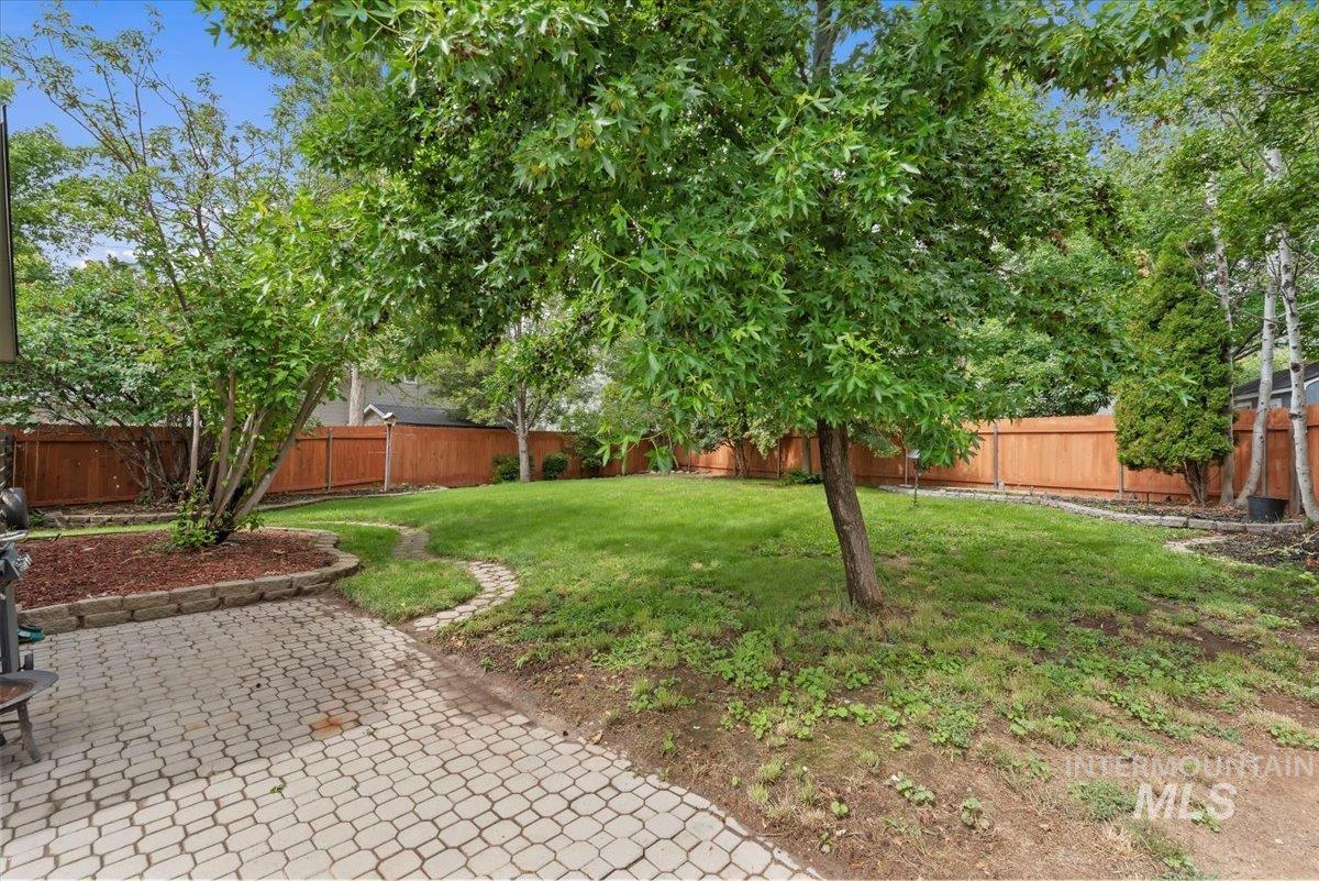 Expansive backyard featuring a paver patio, a manicured lawn, perimeter fencing, mature trees, and established landscaping beds