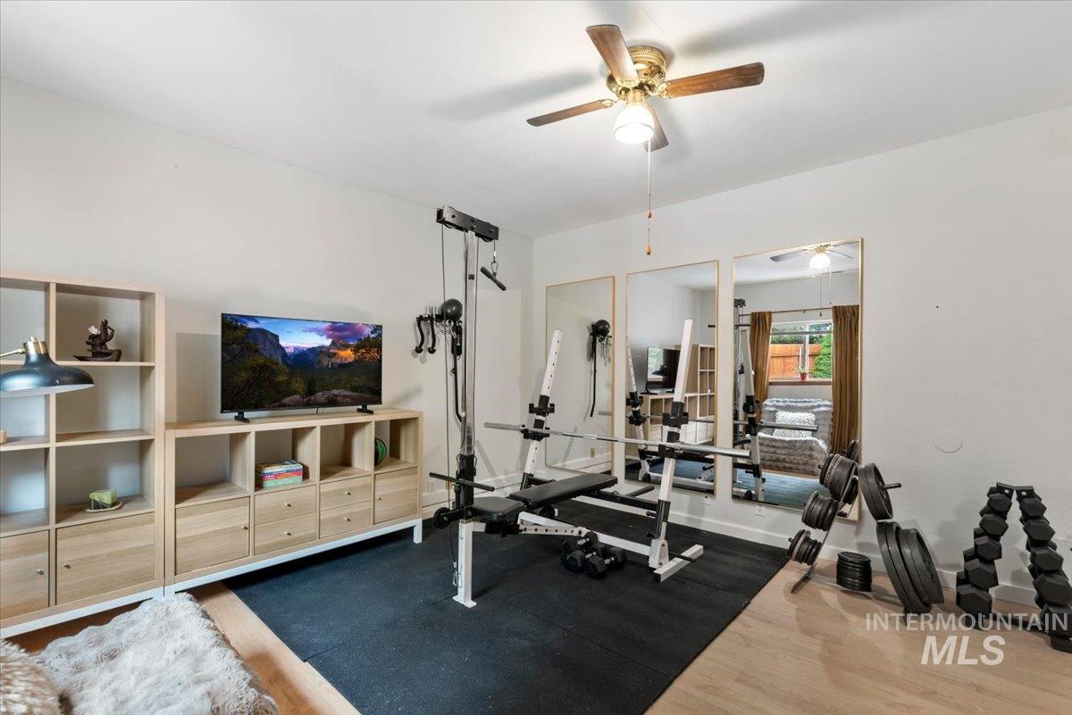 Versatile space featuring light wood-finish flooring, a ceiling fan with integrated lighting, and white wall finishes