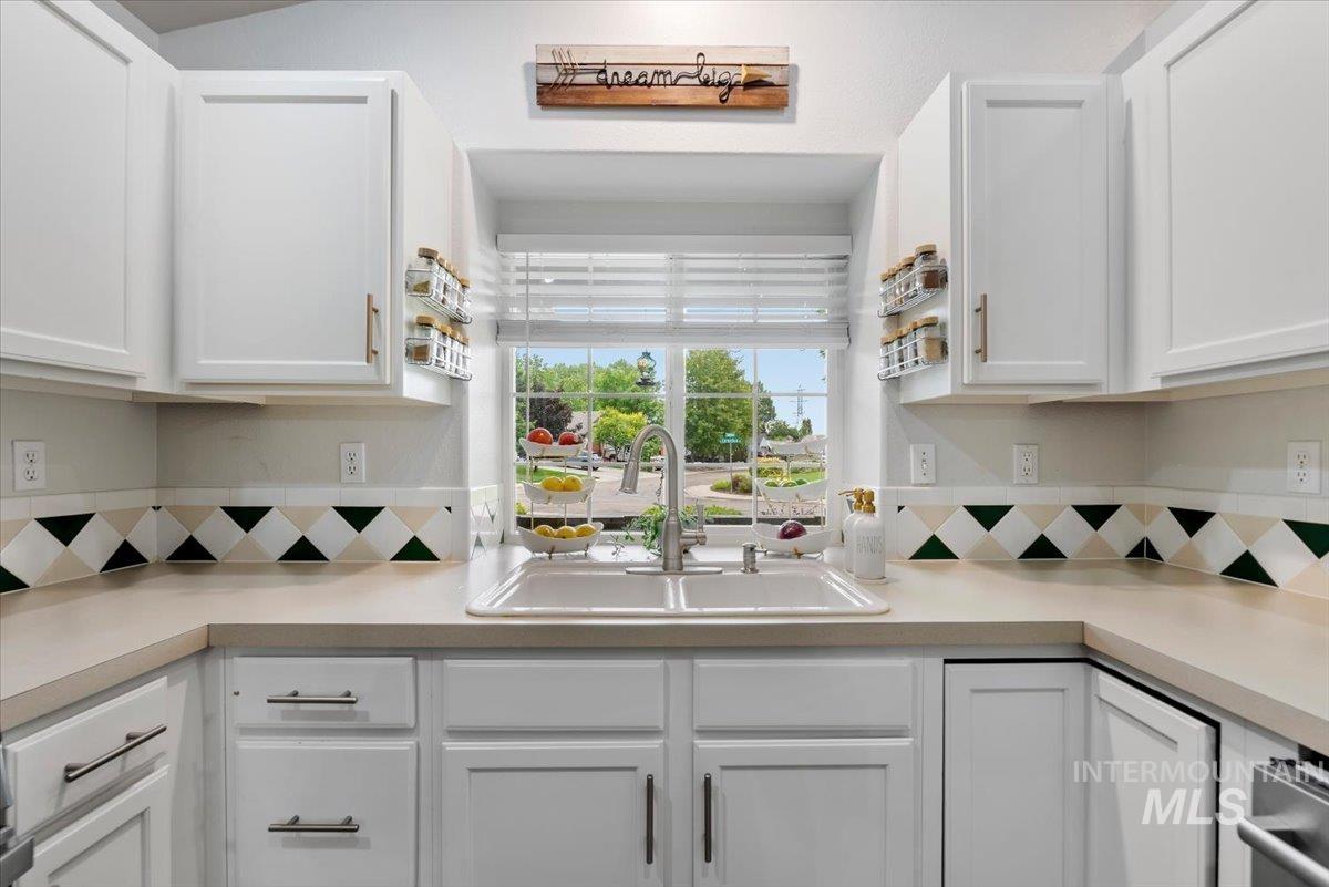 Kitchen featuring a dual-basin sink with a gooseneck faucet, white shaker-style cabinetry, light-toned countertops, and a patterned tile backsplash