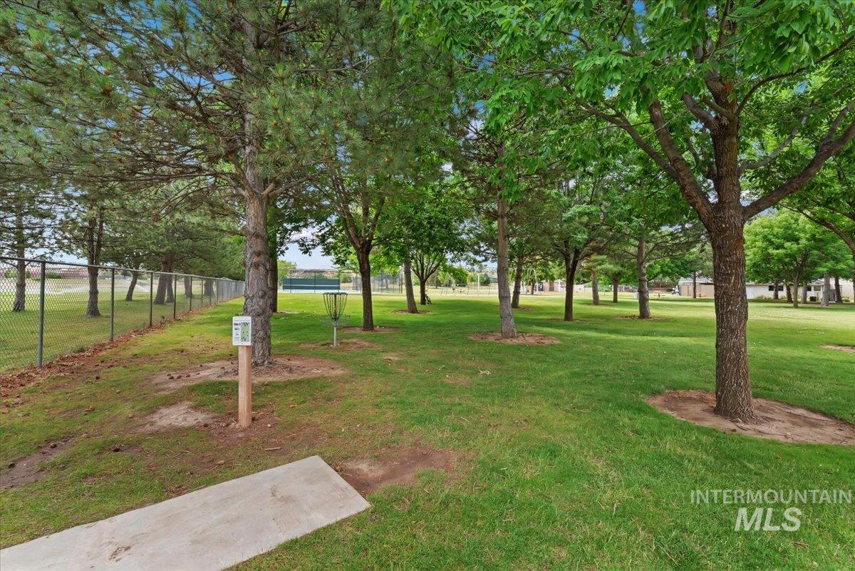 Park-like grounds featuring mature trees, a manicured lawn, chain-link fencing, a concrete tee pad, and a disc golf basket