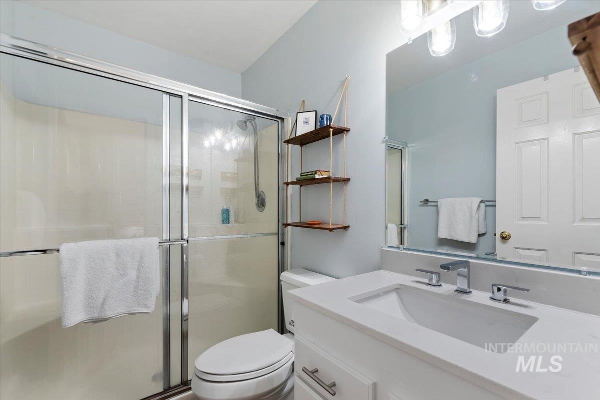 Bathroom featuring a vanity with an integrated sink and chrome fixtures, a large wall-mounted mirror, a three-light vanity bar, a toilet, and a glass-enclosed shower