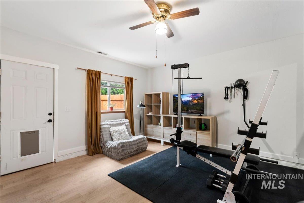 Versatile room featuring wood-finish flooring, a ceiling fan with integrated lighting, and a window with natural light