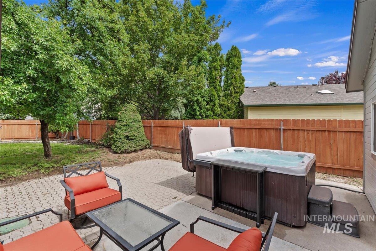 Paved patio with a built-in spa, framed by a wooden privacy fence and mature trees
